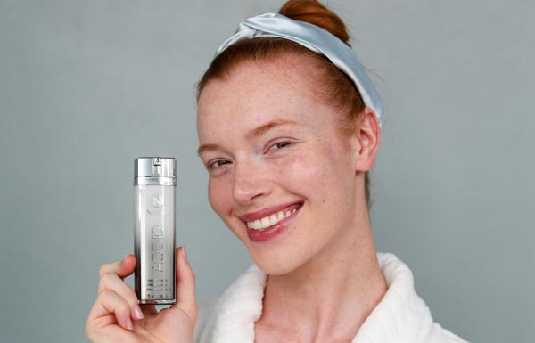Image of woman smiling and holding a bottle of Age IQ Night Cream.