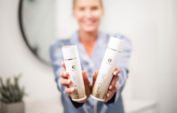Lifestyle shot of a woman holding up the ProLuxe Shampoo and Conditioner bottles.